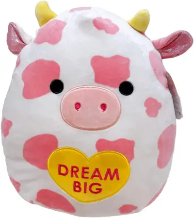 Una vaca rosa i blanca Squishmallow sostenint un cor d'amor groc que diu