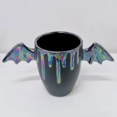 Uma caneca com asas de morcego nas alças e esmalte perolado na borda e nas asas.