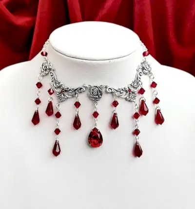 Una collana in argento composta da volute e rose da cui scendono perline di cristallo rosso e gocce.