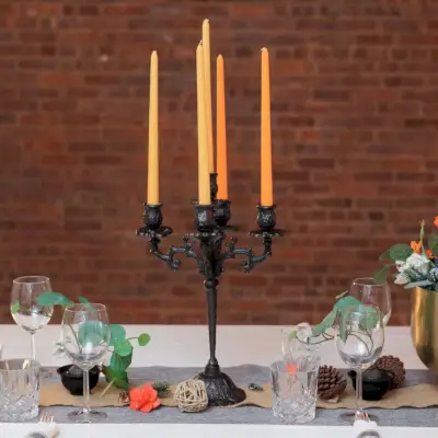 Um candelabro de ferro fundido com velas laranja sobre uma mesa festiva.