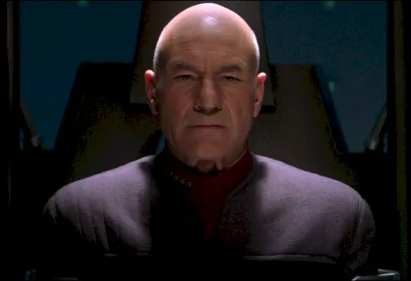 Kapitán Picard v Star Trek Nemesis: Starší holohlavý beloch sa zachmúrene pozerá do kamery.