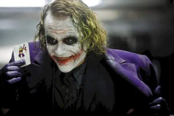 Heath Ledger als Joker, der in Batman: The Dark Knight eine Karte hochhält.