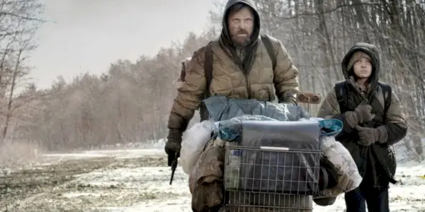 Un père et son fils poussent un caddie sur une route désolée.