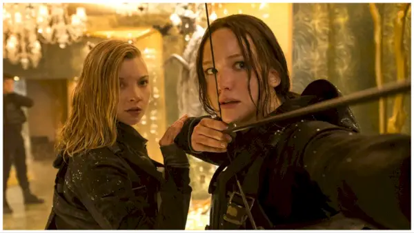 Cressida (Natalie Dormer) en Katniss (Jennifer Lawrence) staan ​​dichtbij terwijl Katniss haar boog van zich af trekt