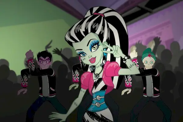 Monster High: New Ghoul a l'escola; Frankie Stein, una persona de pell grisa i cabells blancs i negres, fa el signe de la pau davant d'una multitud fosca.