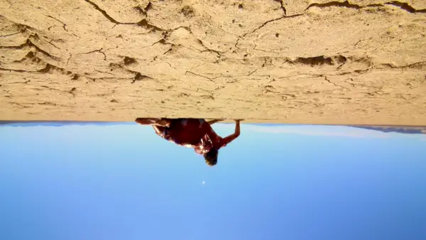 Uma imagem invertida de uma mulher (Michelle May) em um vestido branco ensanguentado enquanto rasteja pelo deserto de Mojave em ‘The Outwaters’.