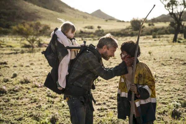 un uomo (Martin Freeman) che indossa uno zaino da trasporto per neonati si accovaccia per parlare con un ragazzino.