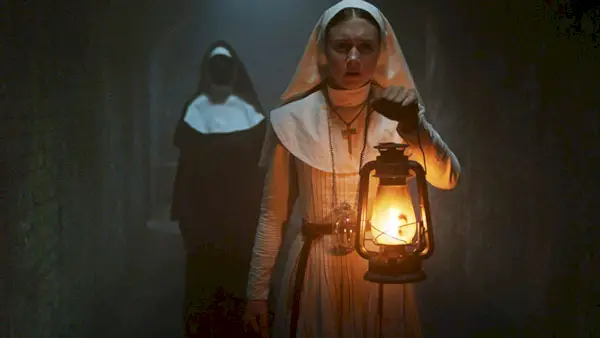 Sestra Irene (Taissa Farmiga) si svieti lampášom na cestu do tmavej chodby, zatiaľ čo mníška bez tváre kráča za ňou.