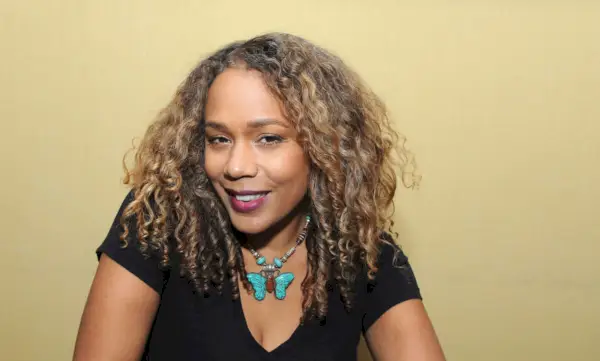 Rachel True smiler, iført en svart skjorte og et turkis sommerfuglkjede.