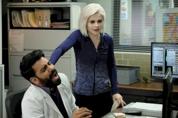 Rahul Kohli som Ravi och Rose McIver som Liv, stående på ett kontor.