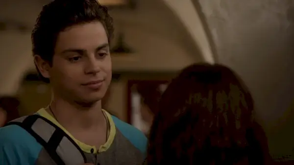 Jake T. Austin porte un t-shirt foncé et un sac à dos à une bretelle