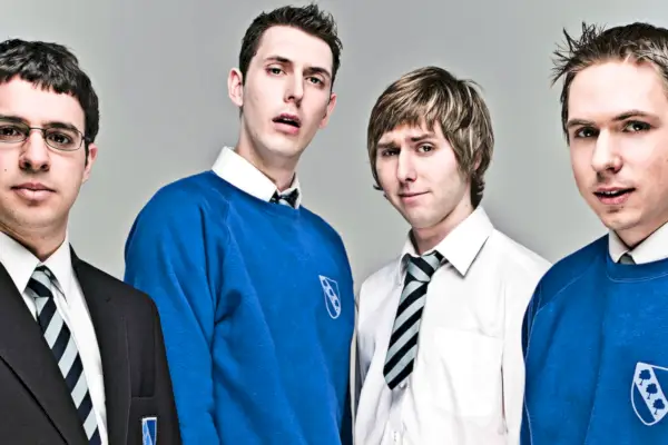 La imagen promocional de Inbetweeners; Simon Bird, Joe Thomas, James Buckley y Blake Harrison, un grupo de adolescentes blancos, están juntos vistiendo un uniforme escolar azul, blanco y negro.