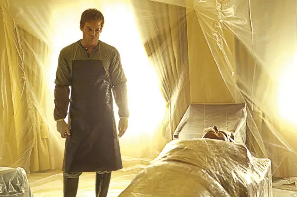 Michael C. Hall como Dexter de pie en una habitación envuelta en plástico con un cuerpo sobre la mesa.