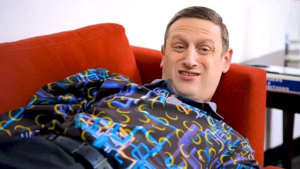 Tim Robinson ligt op een bank en draagt ​​een shirt met een uitgebreid patroon erin