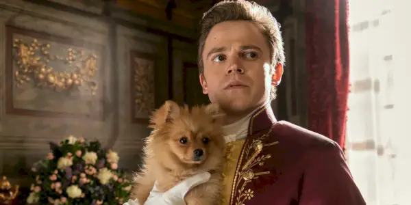 Sam Clemmett som unge Brimsley i Queen Charlotte: A Bridgerton Story som holder en liten Pomeranian-hund