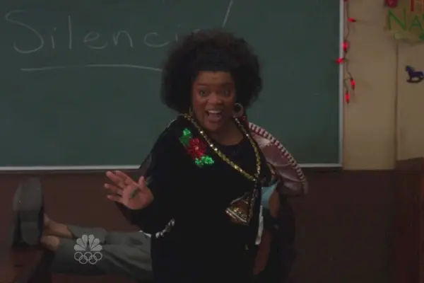 Ainda do episódio comunitário Religião Comparada; Yvette Nicole Brown, uma mulher negra com cabelo natural, fala animadamente enquanto veste um suéter preto de Natal.