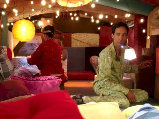 Fotograma del episodio de Community Pillows and Blankets; Danny Pudi se arrodilla dentro de un fuerte de mantas en pijama verde. Allá